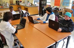 students with laptops at table in classroom