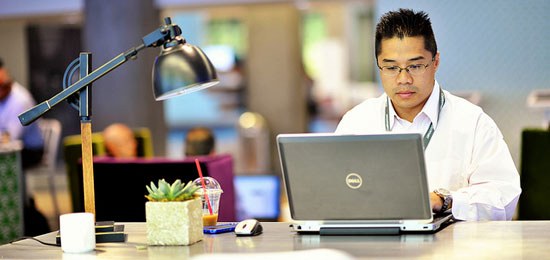 A man sits at a table in a public space using a Dell laptop