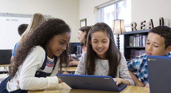 Several elementary school children gather around a Dell laptop in a classroom