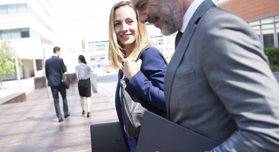Woman and man walk outside office building with Dell Latitude laptops in hand