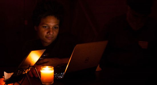 A man works on a Dell laptop by candlelight in a dark room