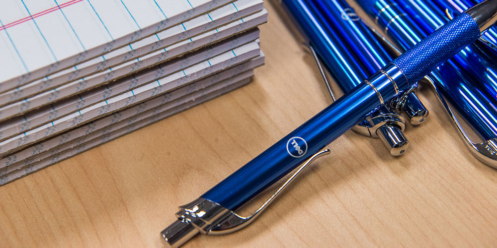 blue ink pens with dell logo next to pads of paper