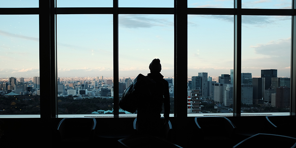 silhouette of person standing in front of windows looking out over a large city