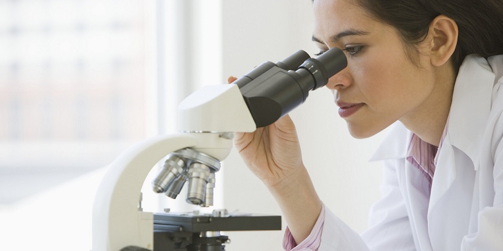 woman in a white coat looking into a microscope