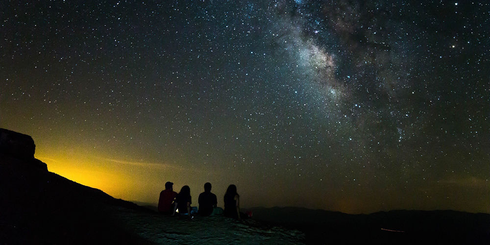 four people sitting outside looking at stars