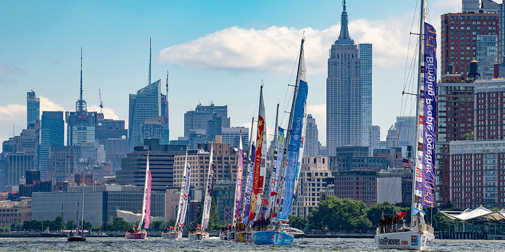 several clipper ships at sail with the skyline of Manhattan behind them