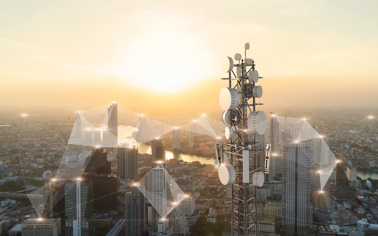 Cell phone tower with a city skyline behind it and graphics indicating connectivity between various locaations.