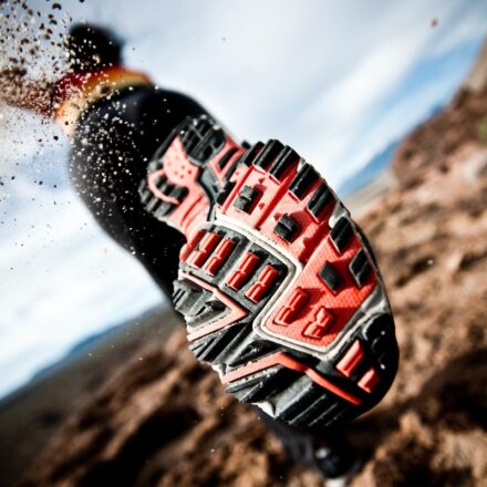 Close up view of the bottom of a running shoe throwing off dirt indicating running fast.
