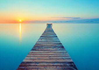 A wooden pier extends over calm water with a sunset in the background.