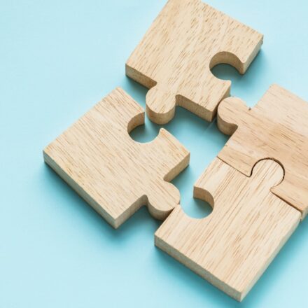 Four wooden puzzle pieces come together to form a square on a light blue background.