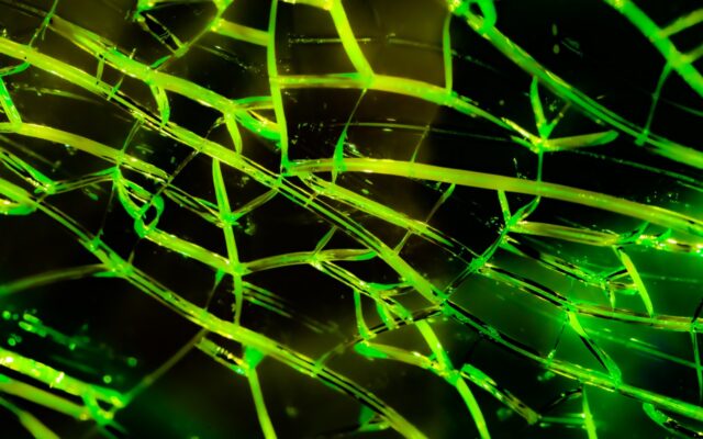 Textured background of green colored cracks in surface against black background.