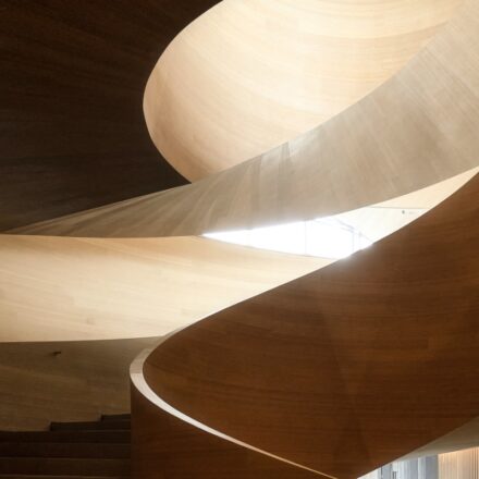 Looking up a curving wooden staircase inside a building.