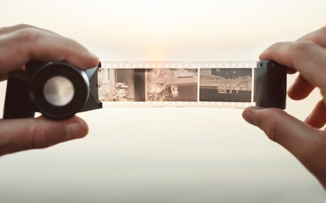 Person holding 35 mm camera film negatives and viewing images with negative viewer lens.