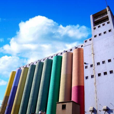 Silos used for industry in different colors with a partly sunny sky in the background.
