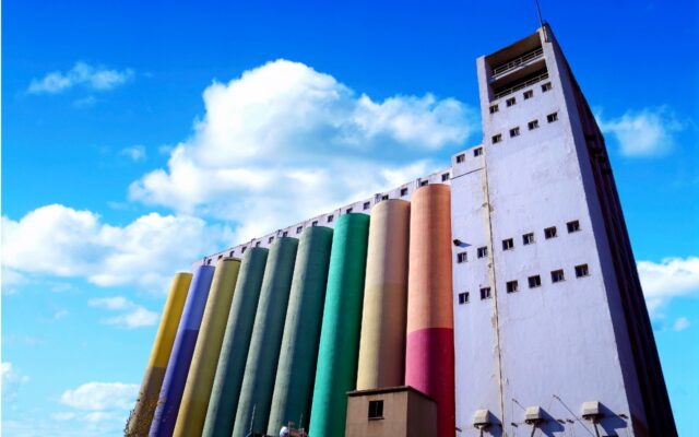 Silos used for industry in different colors with a partly sunny sky in the background.