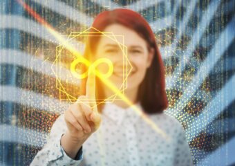 Woman with red hair stands in front of building, holding right index finger out to press DevOps infinity symbol included digitally on image.