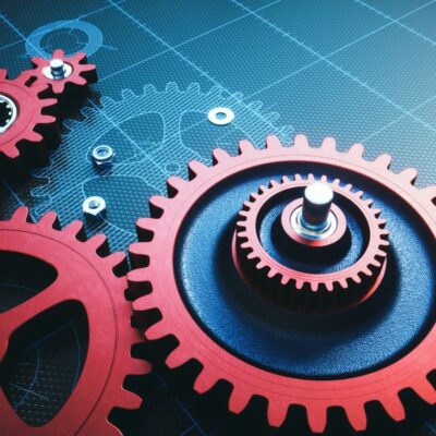 Red metallic gears placed upon a blue grid schematic drawing.