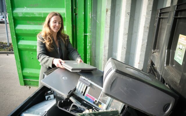 Young woman at an electronics / e-waste collection site, adding an old laptop for recycling.