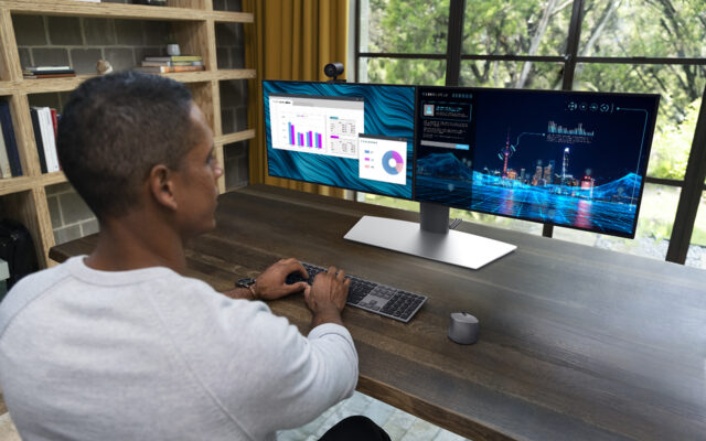 African-American man working from home using dual monitors and wireless mouse and keyboard. Photo taken from over his right shoulder towards the monitors. PC not pictured.