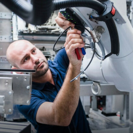 Male technician performing preventative maintenance on a factory robotic arm component..