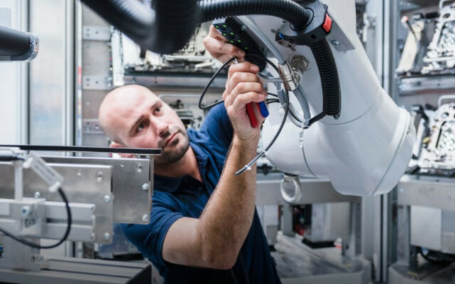 Male technician performing preventative maintenance on a factory robotic arm component..