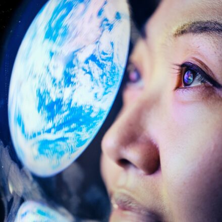 Close up on a female astronaut's face with the reflection of Earth on her helmet's faceshield.