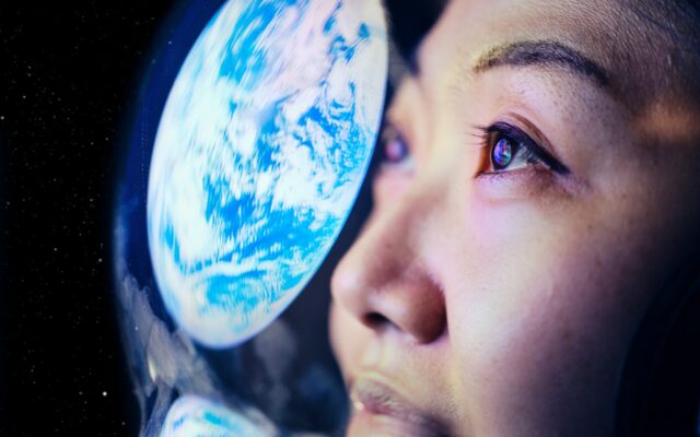 Close up on a female astronaut's face with the reflection of Earth on her helmet's faceshield.