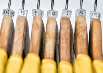 Yellow womens' t-shirts on hangers with sizing labels indicating sizes from XS to XL, as read from left to right.