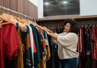 An African-American woman is looking through a rack of clothes in a retail store.