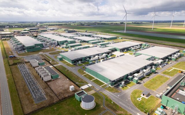 Aerial view of a data center with wind turbines nearby.