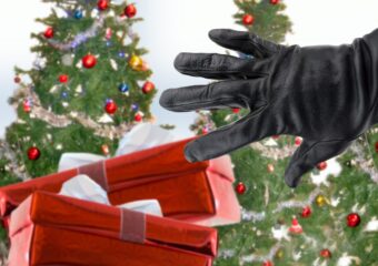 Gloved hand reaching for holiday gifts, with decorated Christmas trees in the background.