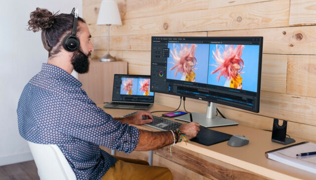 A male photo editor works using a desk setup with the Dell UltraSharp 34 Curved USB-C Hub Monitor (U3423WE).