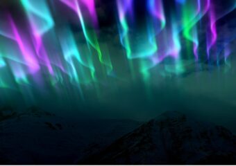 A view of the multiple colors of the Aurora Borealis or Northern Lights over a mountain range.