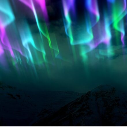 A view of the multiple colors of the Aurora Borealis or Northern Lights over a mountain range.