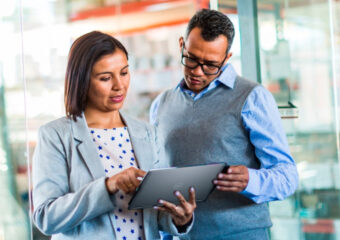 Female (l) and male (r) coworkers review business data in the office on a Dell Latitude 14 7000 Series touch tablet.