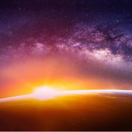 Digitally rendered image of sun emerging over Earth's horizon, light breaking and Milky Way galaxy in background. Image created digitally based on elements furnished by NASA.
