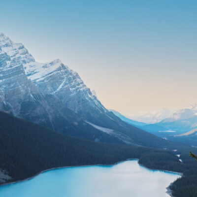 Landscape photo of lake in a mountain range, with a pink and blue daylight sky in the background.