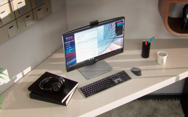 Dell Optiplex 7400 AIO thin client on desk with keyboard, mouse, headphones and writing notebook.