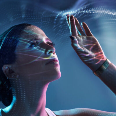 Young Caucausian woman holds her left hand up as high tech effects appear around her fingers and reflect on her face.