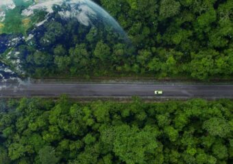 Ariel view of an electric vehicle (EV) driving on a road through a forest with Earth super-imposed over the forest canopy.
