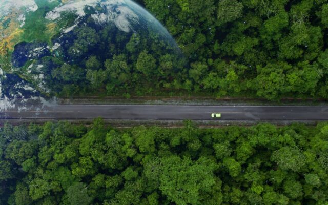 Ariel view of an electric vehicle (EV) driving on a road through a forest with Earth super-imposed over the forest canopy.