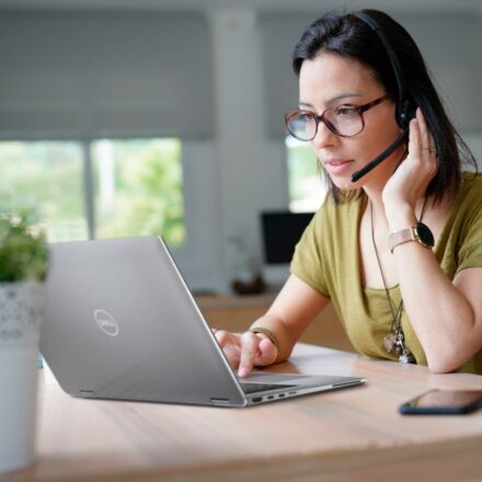 Young woman with glasses and a headset takes part in a meeting remotely using her Dell Latitude 9510 laptop.