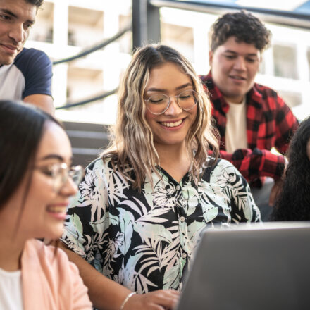 Young woman showing something on the laptop to her friends on university stairs