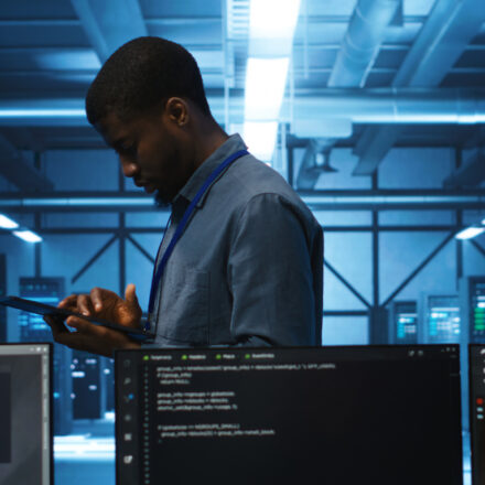 Technician doing system analysis using tablet, doing needed adjustments in supercomputers server farm. Engineer overseeing data center housing storage infrastructure supporting critical IT workloads