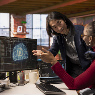 CTO manager in multiethnic startup office helps technician coding advanced AI algorithm and machine learning models. Team leader overseeing work done by employee in Silicon Valley workplace