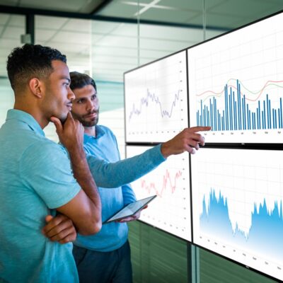 Two male colleagues in an office looking at reviewing various reports projected on to four Dell UltraSharp U2718Q monitors.