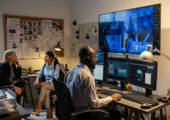 human side of security Young African American FBI agent sitting in front of computer monitors and screen in office while watching security camera records