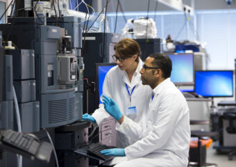 Dell PowerEdge for AI research. Scientists in a laboratory recording data. Both working beside a special piece of machinery called a Mass spectrometry (MS) , an analytical chemistry technique that helps identify the amount and type of chemicals present in a sample by measuring the mass-to-charge ratio and abundance of gas-phase ions